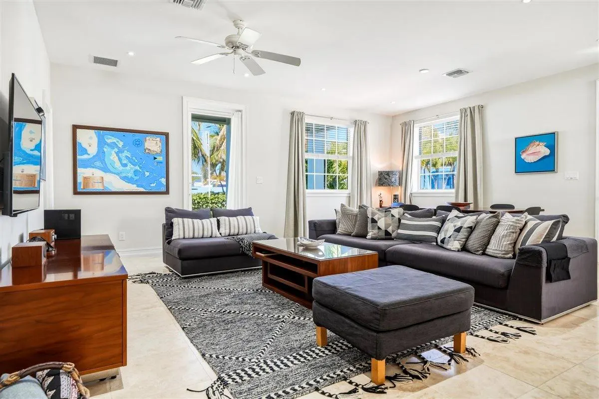 Living room with gray sofas, a wood coffee table, and a black and white patterned rug. Windows offer views of palm trees and blue water.