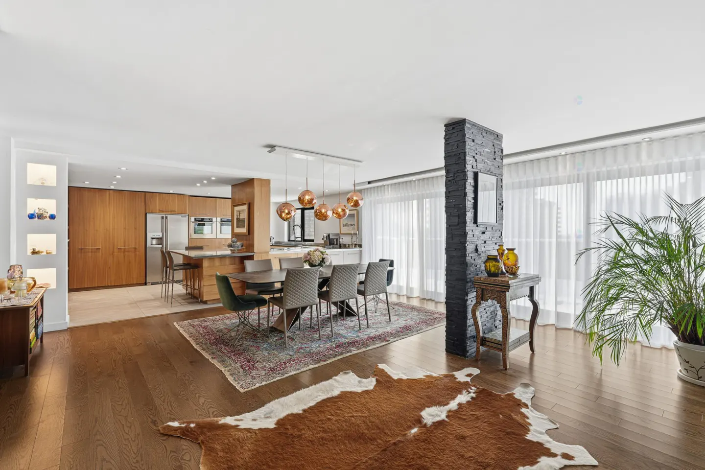 Open-concept living space with wood floors, dining table, kitchen island, and a brown and white cowhide rug.