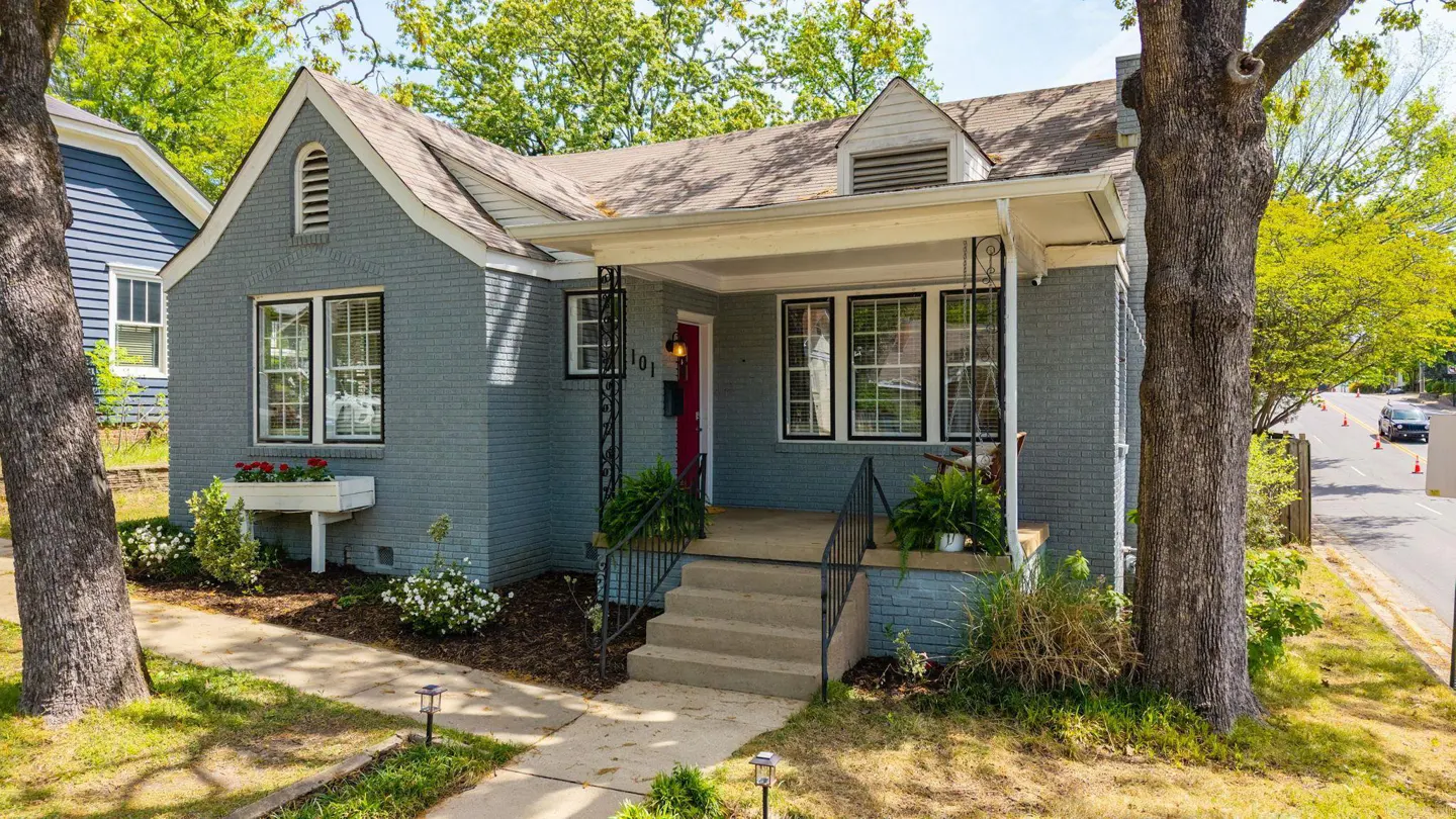 A gray brick house with a red door and a small porch with black railings.