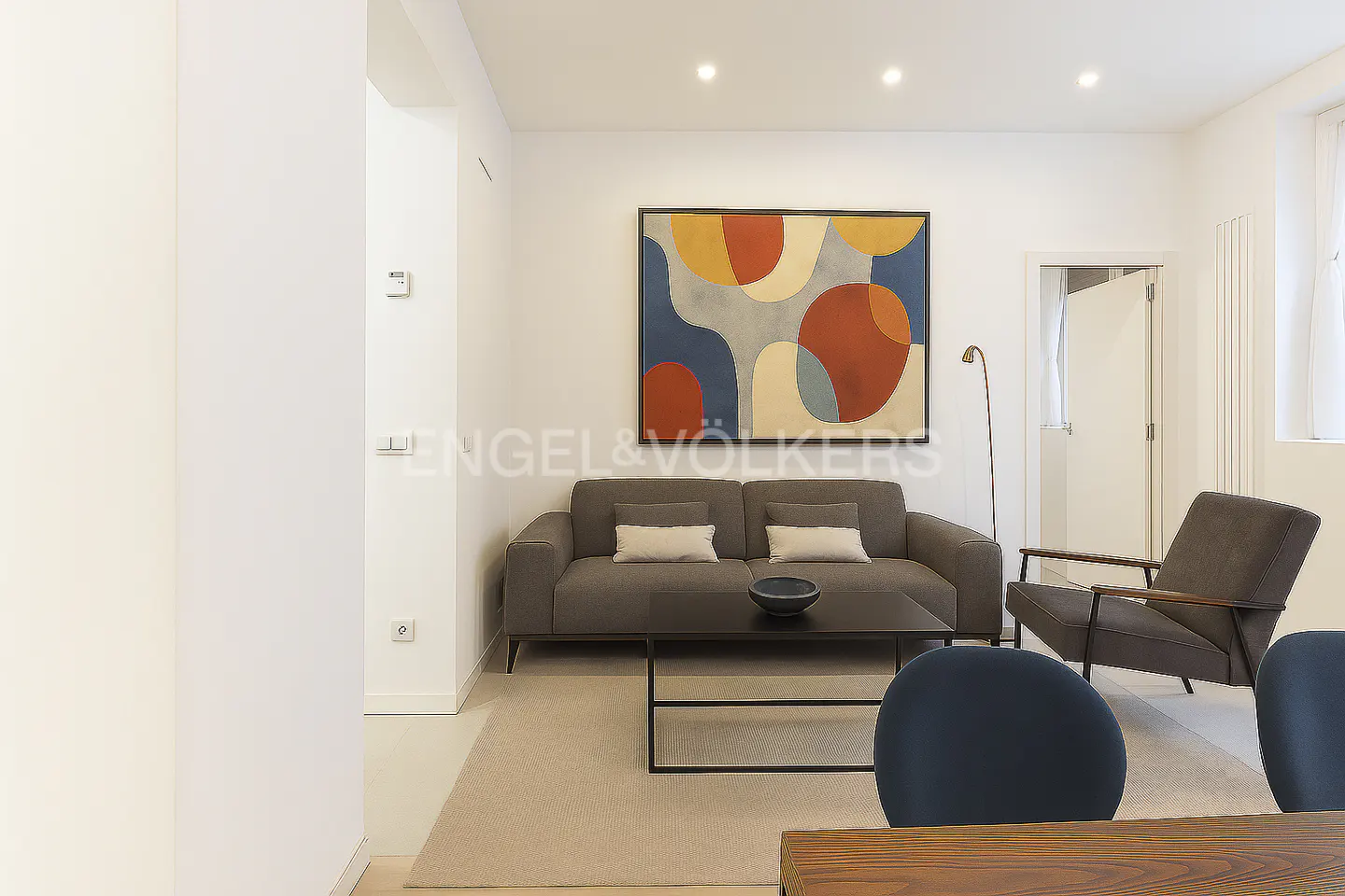 Living room with gray sofa, armchair, and abstract art. A black coffee table sits in front of the sofa. The walls are white.
