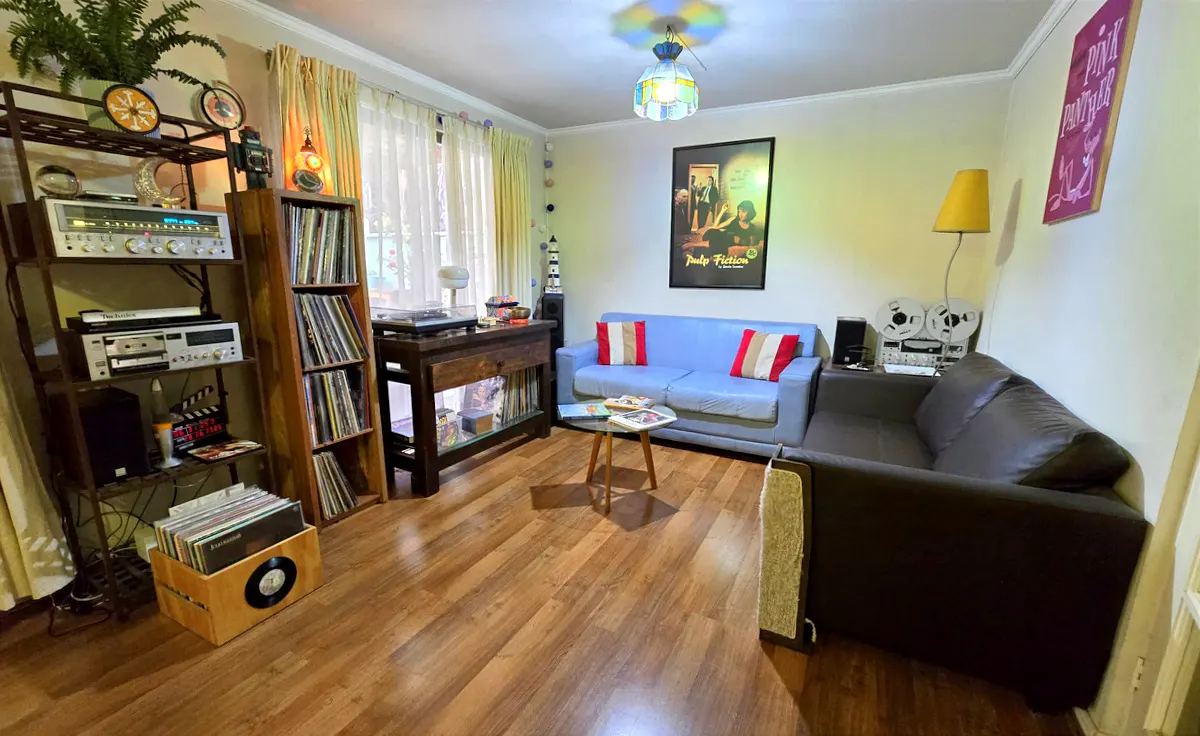 Living room with wood floors, blue and brown sofas, record player, and "Pulp Fiction" poster.