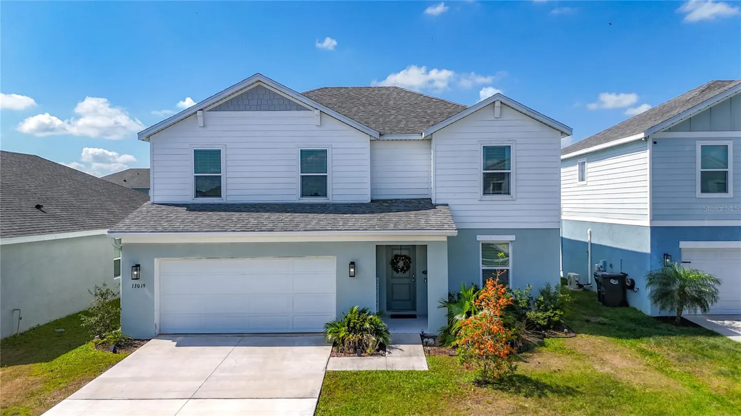 Two-story house with white siding, light blue trim, gray roof, and a white garage door on a sunny day.
