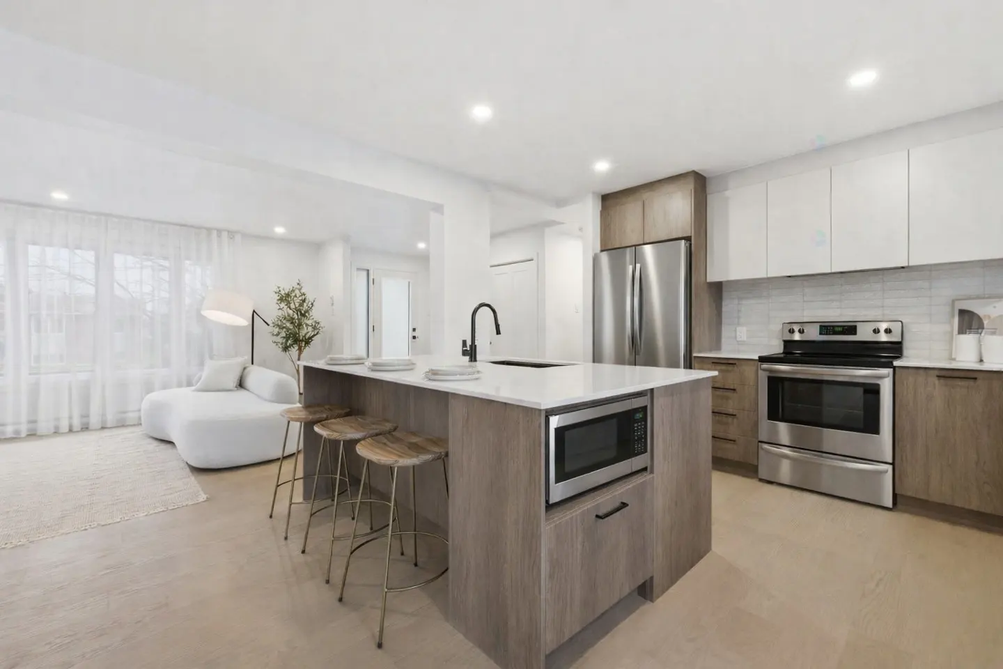 Bright, modern kitchen with a large island, stainless steel appliances, and white cabinets. A white sofa sits in the background.