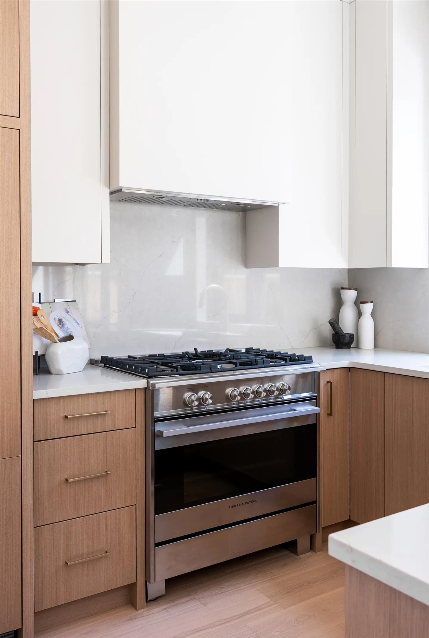A modern kitchen features a stainless steel range oven, light wood cabinets, and white countertops.