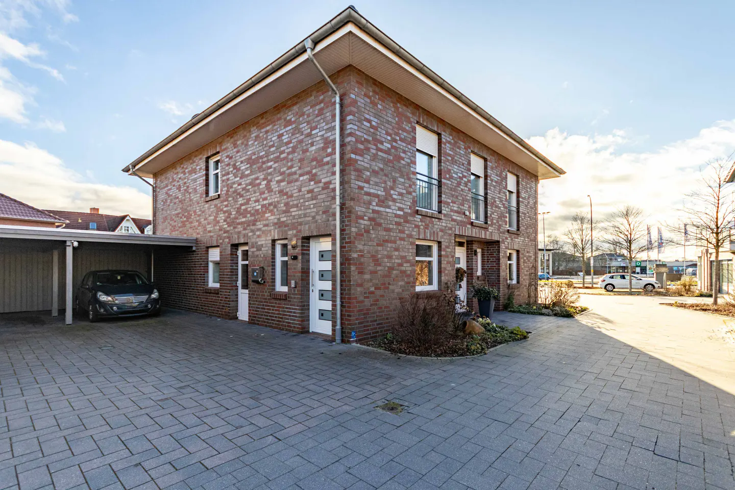 Two-story brick duplex with a gray brick driveway and a carport with a black car parked inside.