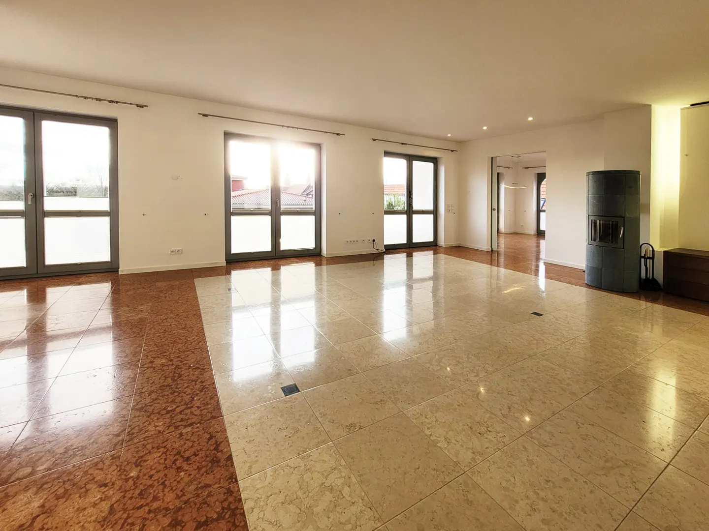 Bright, empty room with marble floors, white walls, and three sets of glass doors. A gray fireplace stands in the corner.