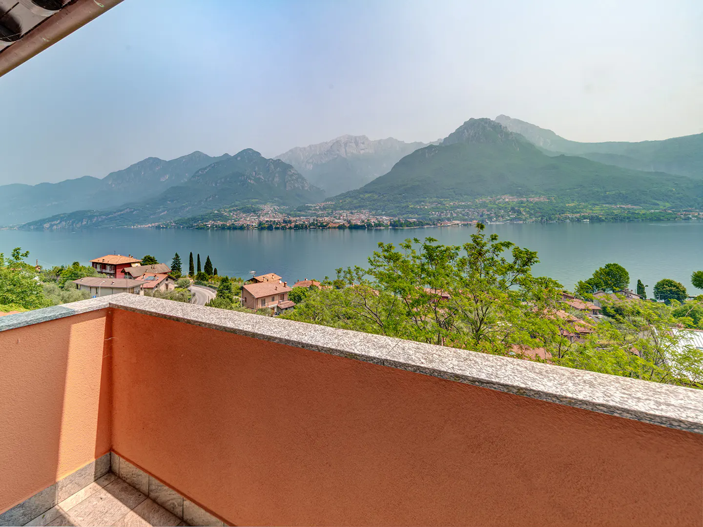 View from a balcony with an orange wall overlooking a lake, mountains, and houses.