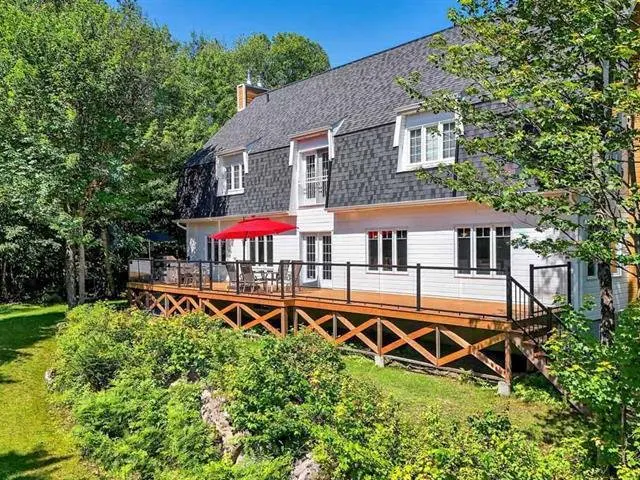 Exterior view of a white house with a gray roof and a wooden deck with a red umbrella.