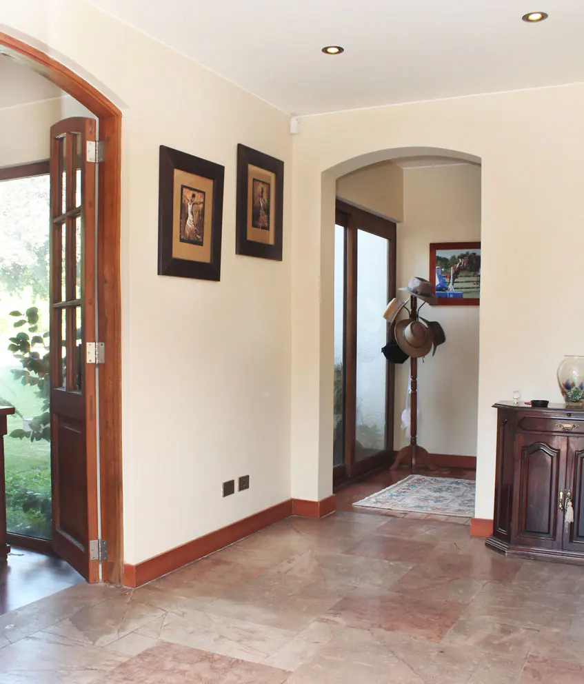 Interior view of a home with light beige walls, brown trim, and tile floors. Two framed pictures hang on the wall. A wooden door is open to the outside.