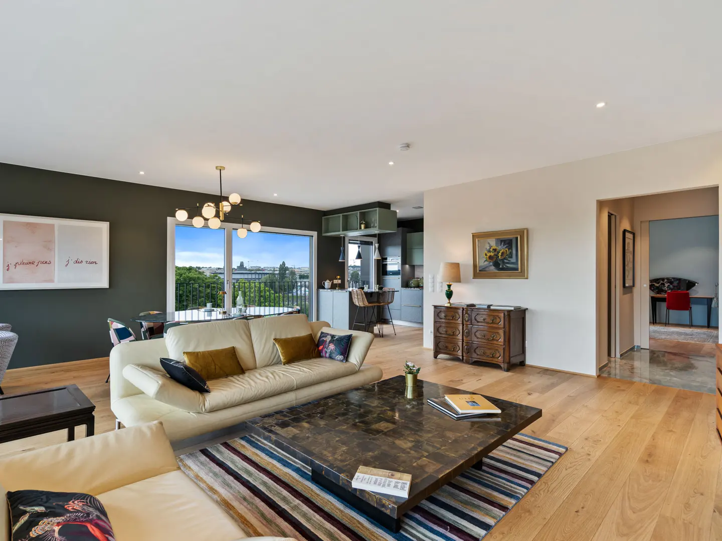 Open-concept living room with hardwood floors, cream sofas, and a dark marble coffee table. Kitchen and balcony visible.