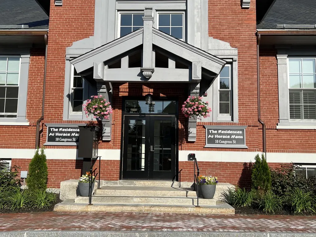 Exterior of "The Residences At Horace Mann" building with brick facade, gray trim, black doors, and flower baskets.