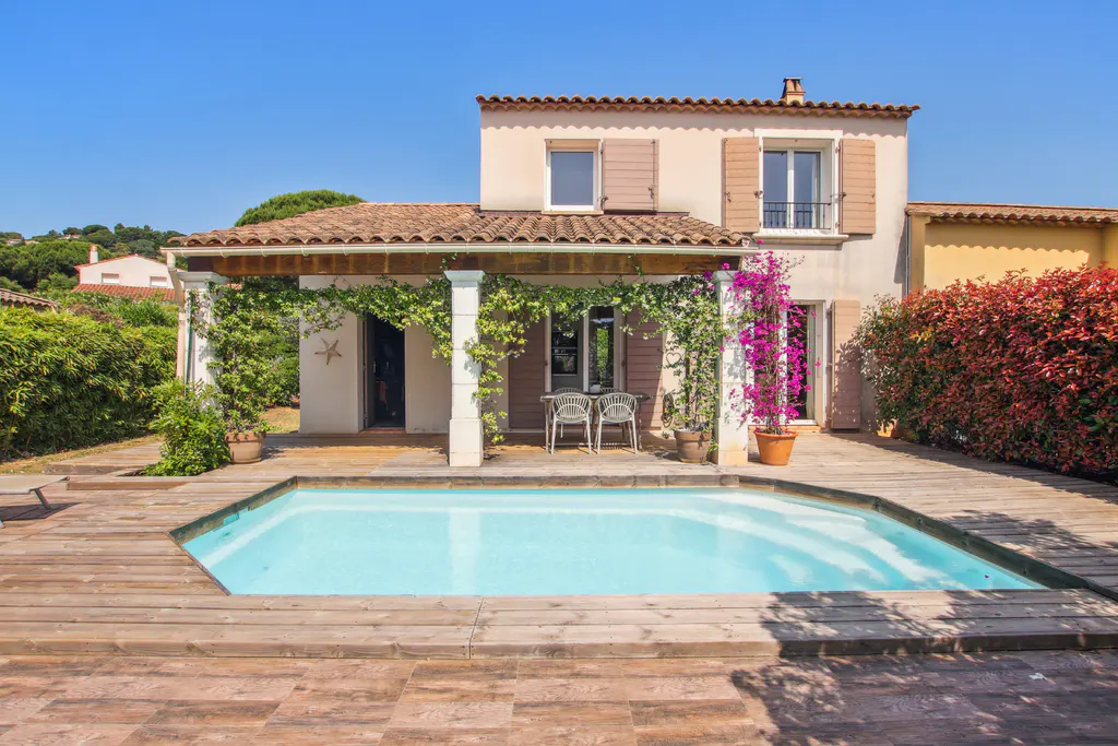 A two-story Mediterranean-style house with a wooden deck, swimming pool, and a covered patio with dining furniture.
