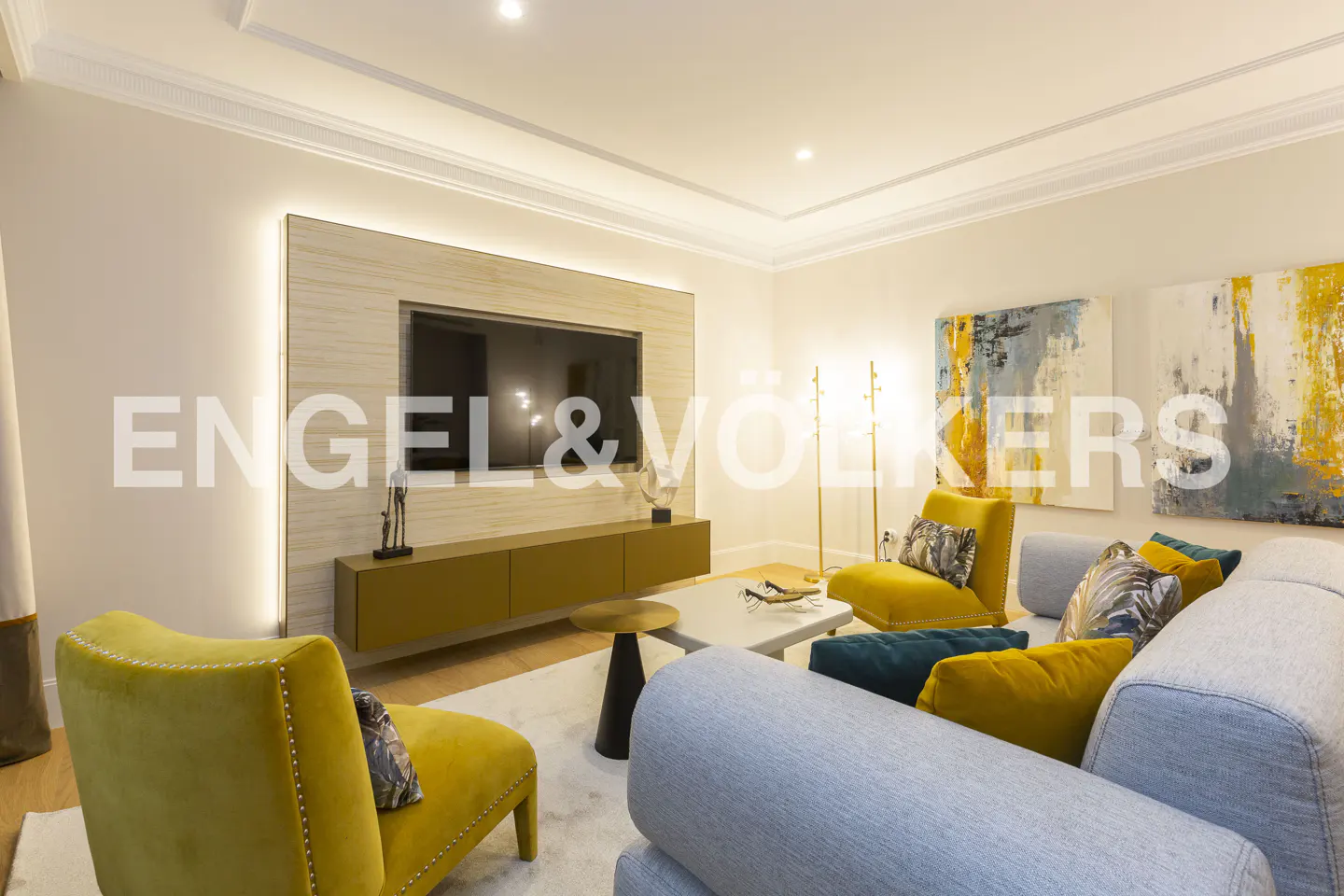 Living room with yellow chairs, a gray sofa, and abstract art. A TV is mounted above a console table.