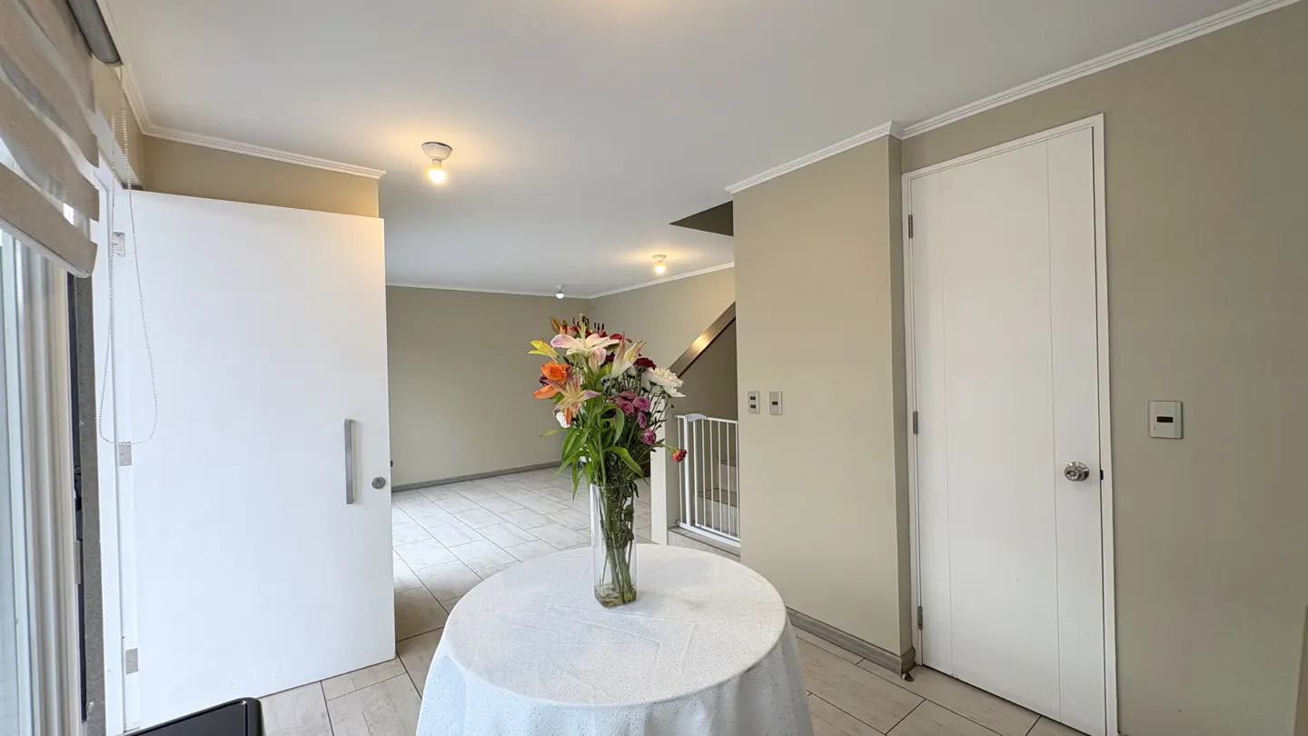 Entryway with a round table covered with a white cloth and a vase of colorful flowers. White doors and beige walls.