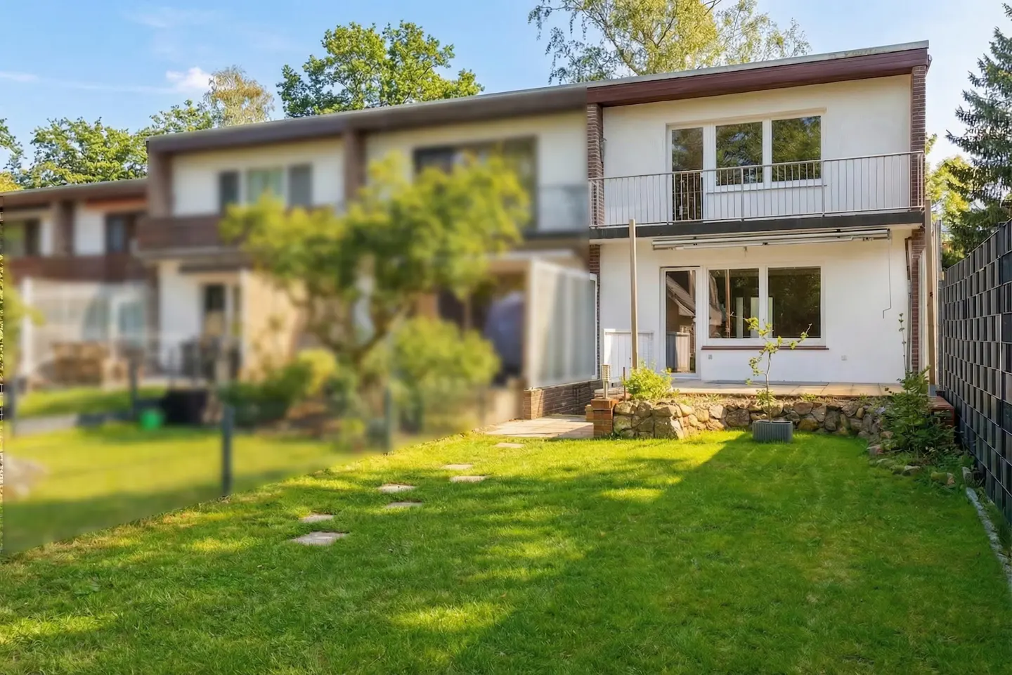 Two-story white house with a balcony overlooking a green lawn with stone pavers. Trees in the background.