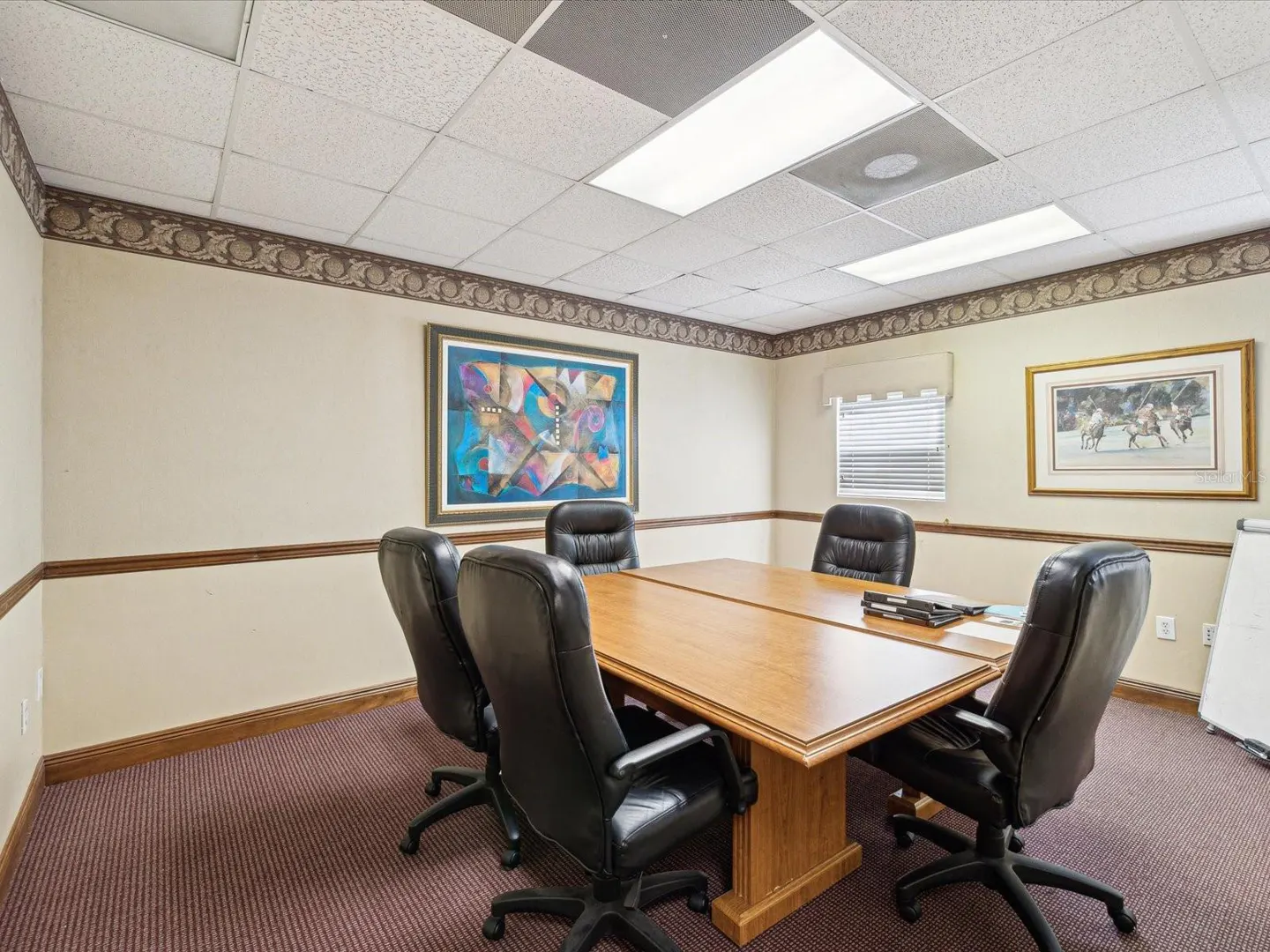 Conference room with a wood table, black leather chairs, and beige walls with decorative trim. Artwork hangs on the walls.