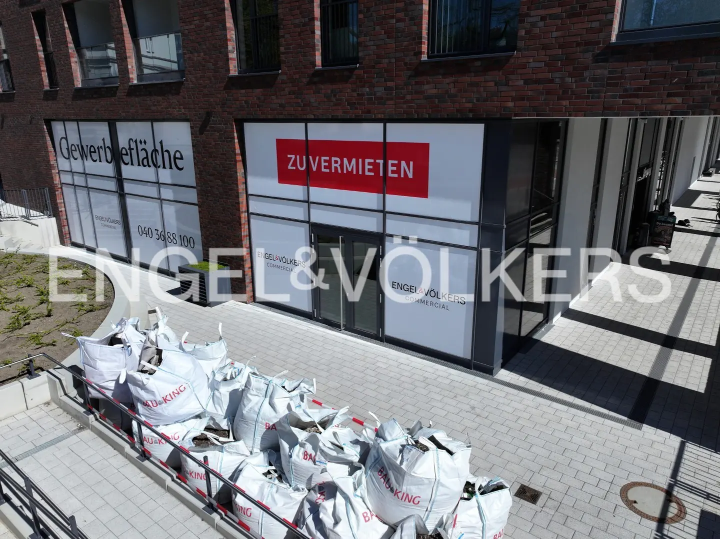 Exterior view of an Engel & Völkers commercial space with a "ZU VERMIETEN" sign. Bags of construction debris are in the foreground.