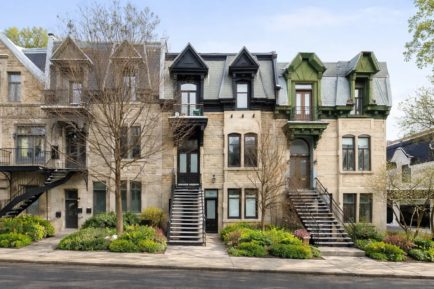 Row of three-story stone townhouses with exterior staircases and dormer windows, set against a blue sky.