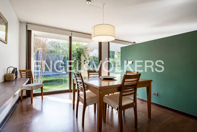 A dining room with a wooden table, chairs, and a view of a green garden through a large window.