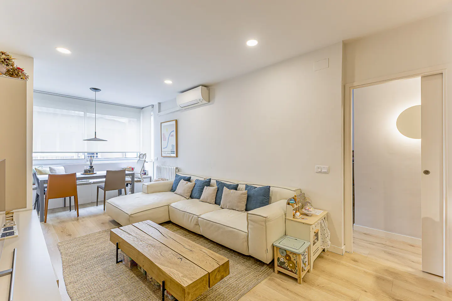 Modern living room with a white sectional sofa, wooden coffee table, and dining area with light wood floors.