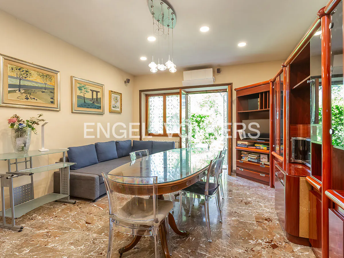 A living room with a glass table, clear chairs, a gray sofa, and a wooden cabinet on a marble floor.
