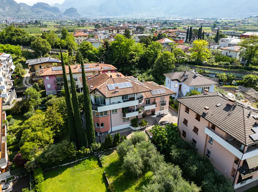 Aerial view of pink apartment buildings with solar panels, surrounded by lush trees and a valley with mountains in the back.