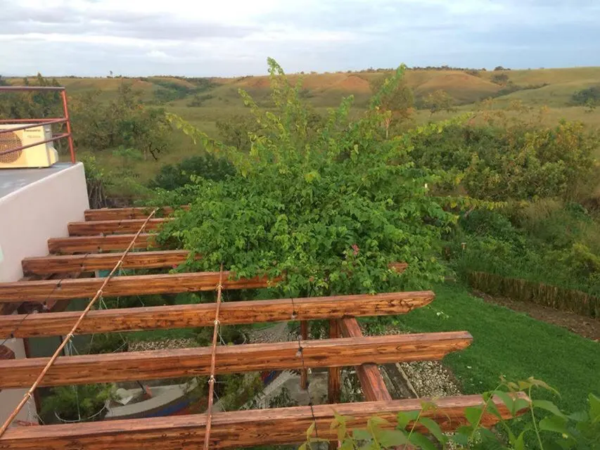 View from a patio with a wooden pergola, overlooking green hills and a cloudy sky.