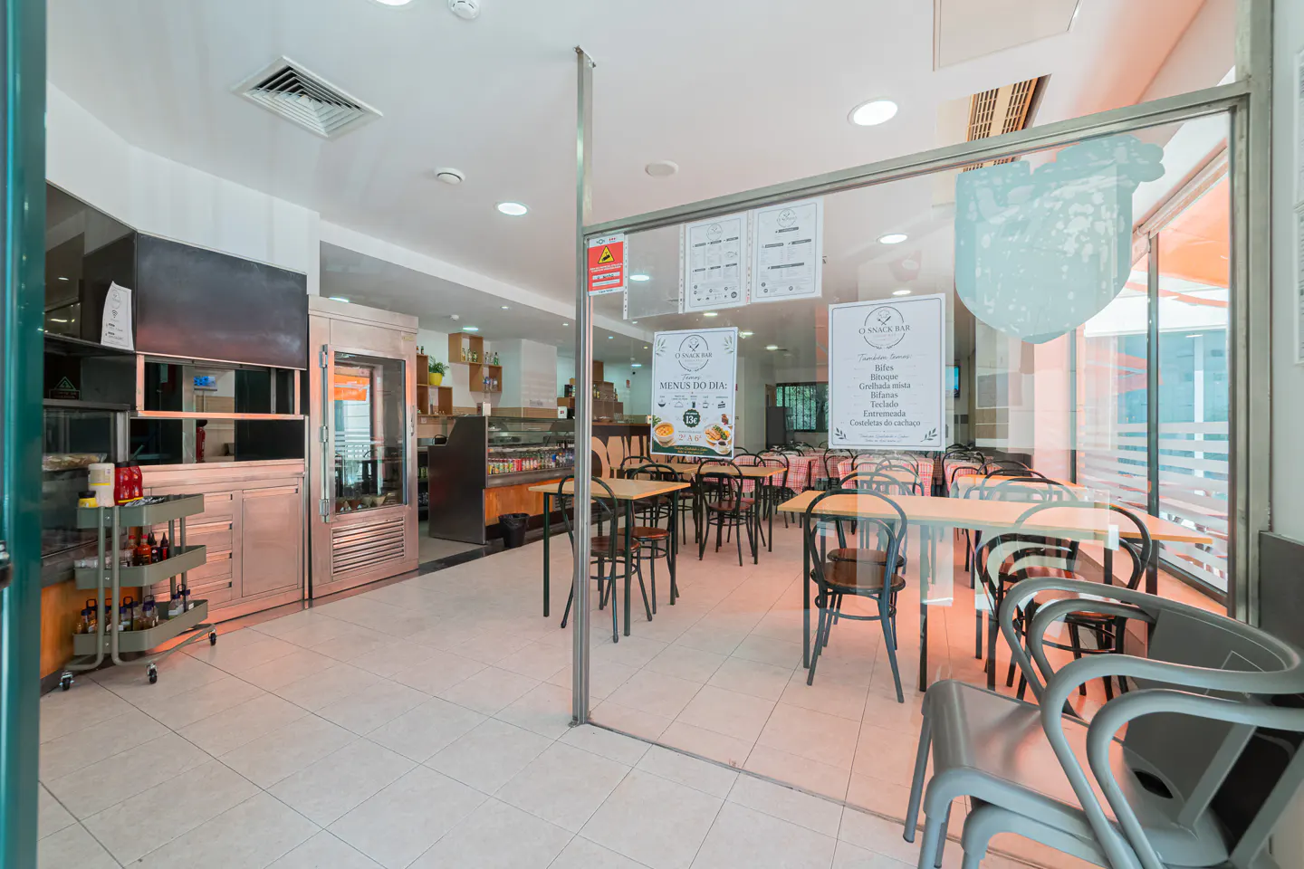 View of a bright, modern restaurant interior with tables, chairs, and a glass-enclosed dining area.