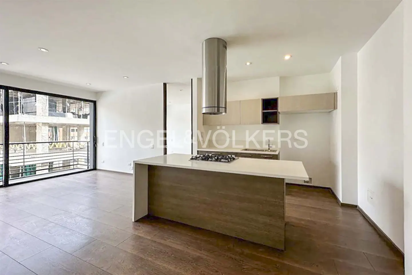 A bright, modern kitchen with wood floors, a large island, and stainless steel appliances. A large window overlooks a balcony.