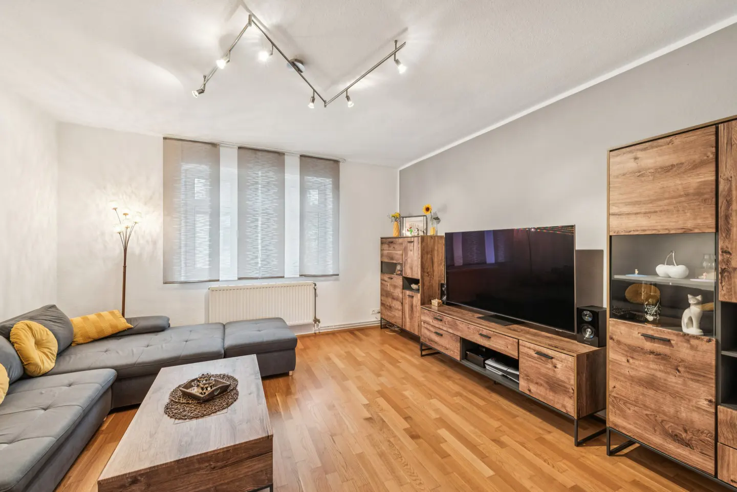 Living room with gray sofa, wood floors, and entertainment center. Sunlight streams through the window.