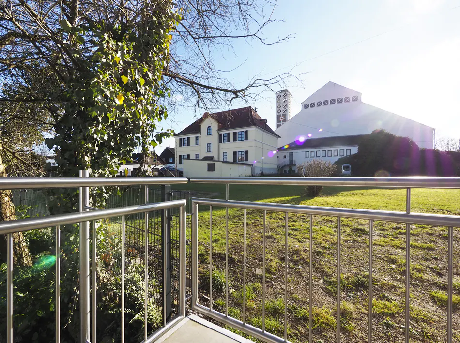 View from a balcony with metal railings, overlooking a grassy area with buildings in the background.