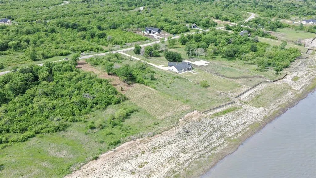 Aerial view of a waterfront property with a house, green trees, and a sandy shoreline.