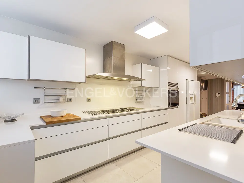 Bright, modern kitchen with white cabinets, stainless steel hood, and island. A gas cooktop sits on the counter.