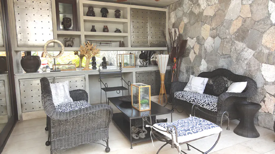 A sunroom with stone walls and wicker furniture. A black coffee table sits in the center, with shelves and decor in the background.