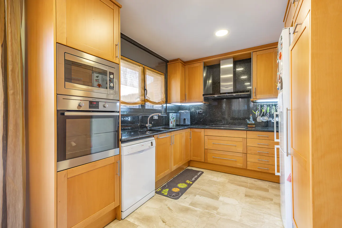 A kitchen with light wood cabinets, black granite countertops, and stainless steel appliances. A white dishwasher is next to the oven.
