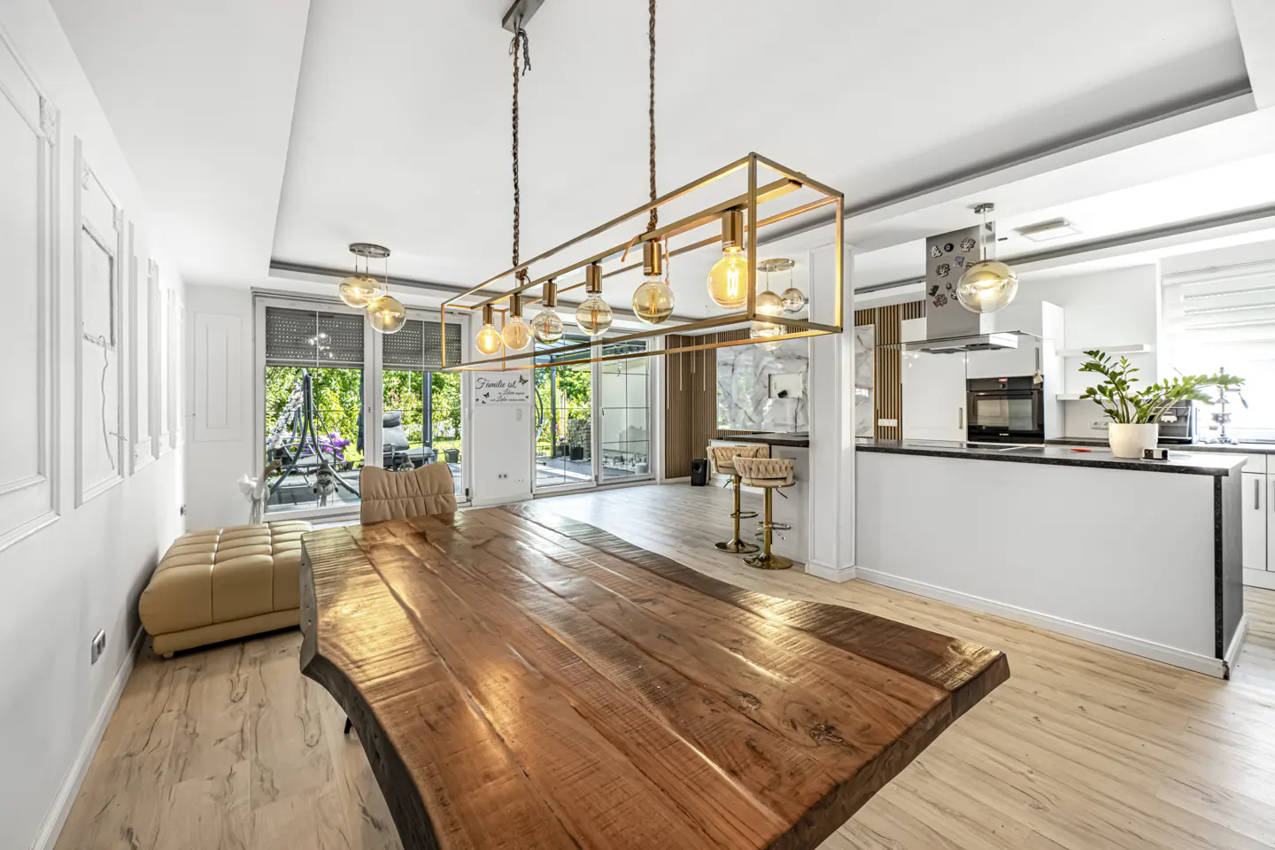 Modern dining room with a live-edge wood table, gold rectangular pendant light, and an open-concept kitchen in the background.