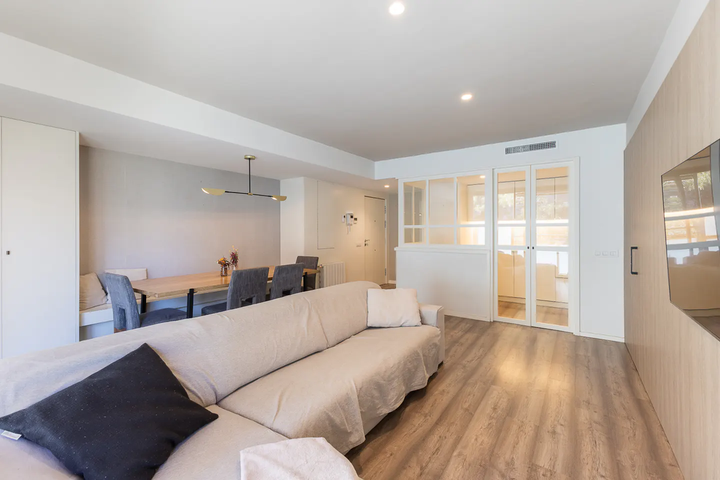 Living room with a beige sofa, a wooden dining table with gray chairs, and a glass-paneled door.