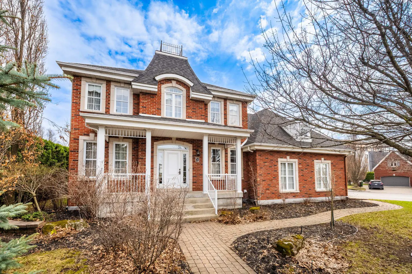 Two-story red brick house with white trim, a porch, and a black roof under a blue sky.
