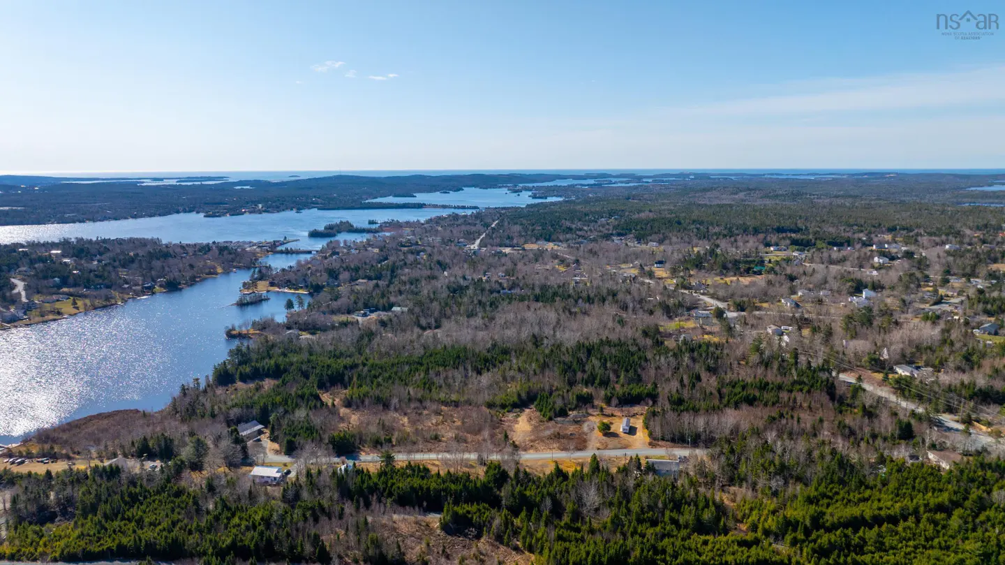 Aerial view of a wooded area with a lake and scattered houses under a clear blue sky.