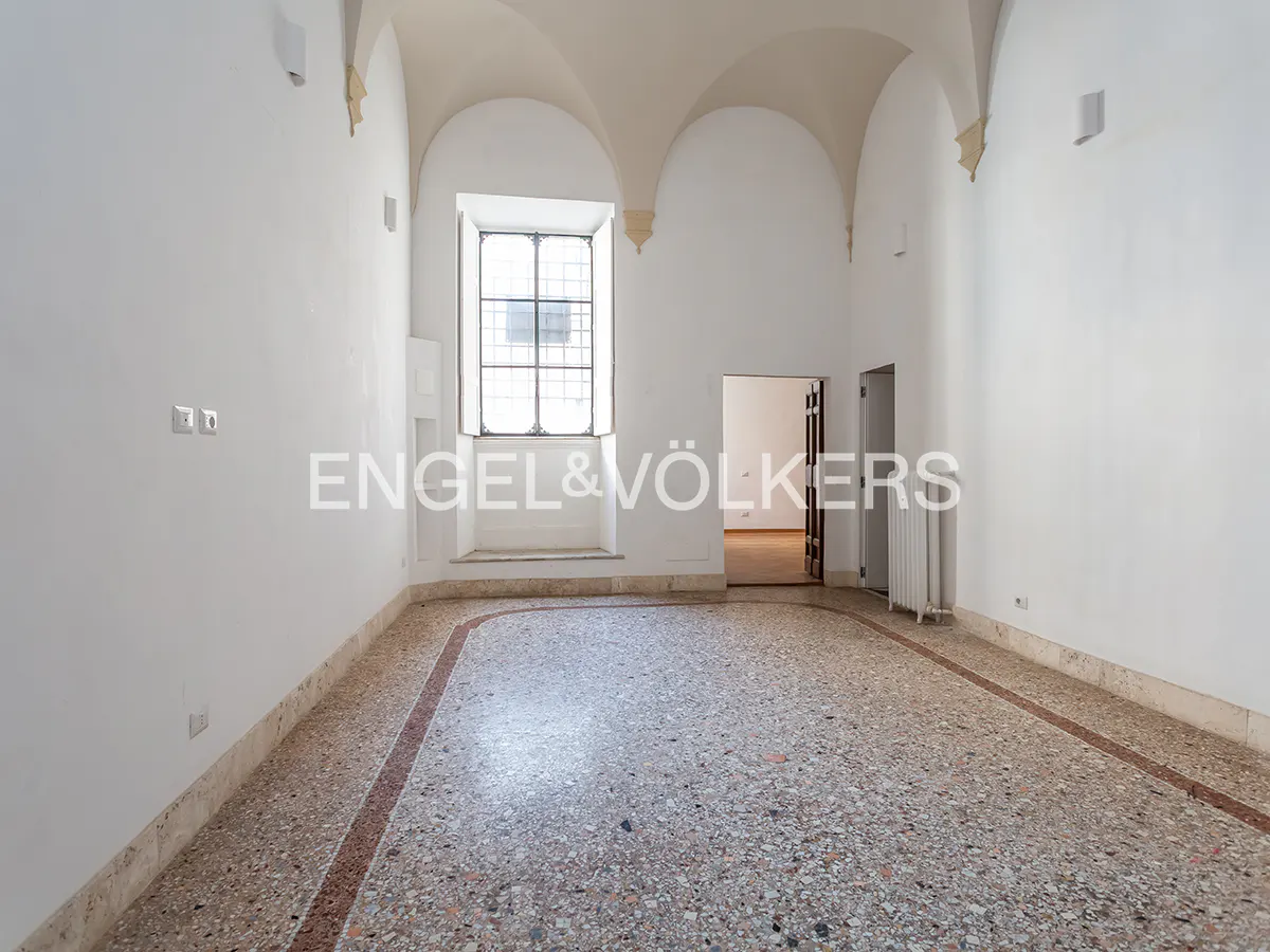 Empty white room with arched ceiling, terrazzo floor, and a window with black grilles. Doorway to another room is visible.