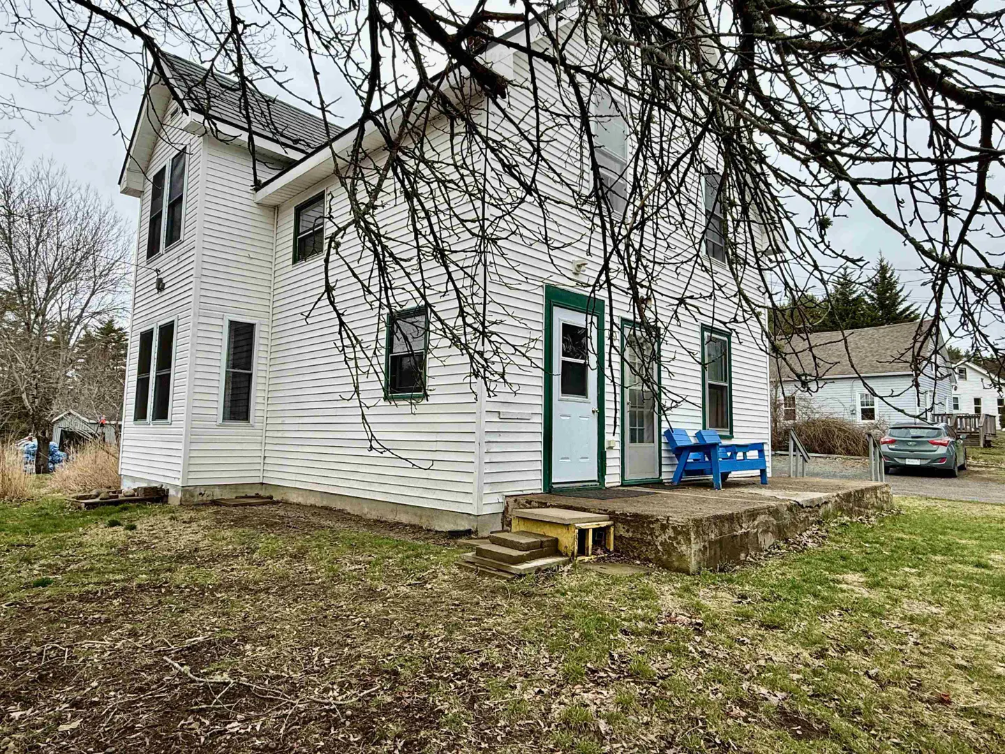 Two-story white farmhouse with green trim, blue bench on porch, and bare tree branches in foreground.