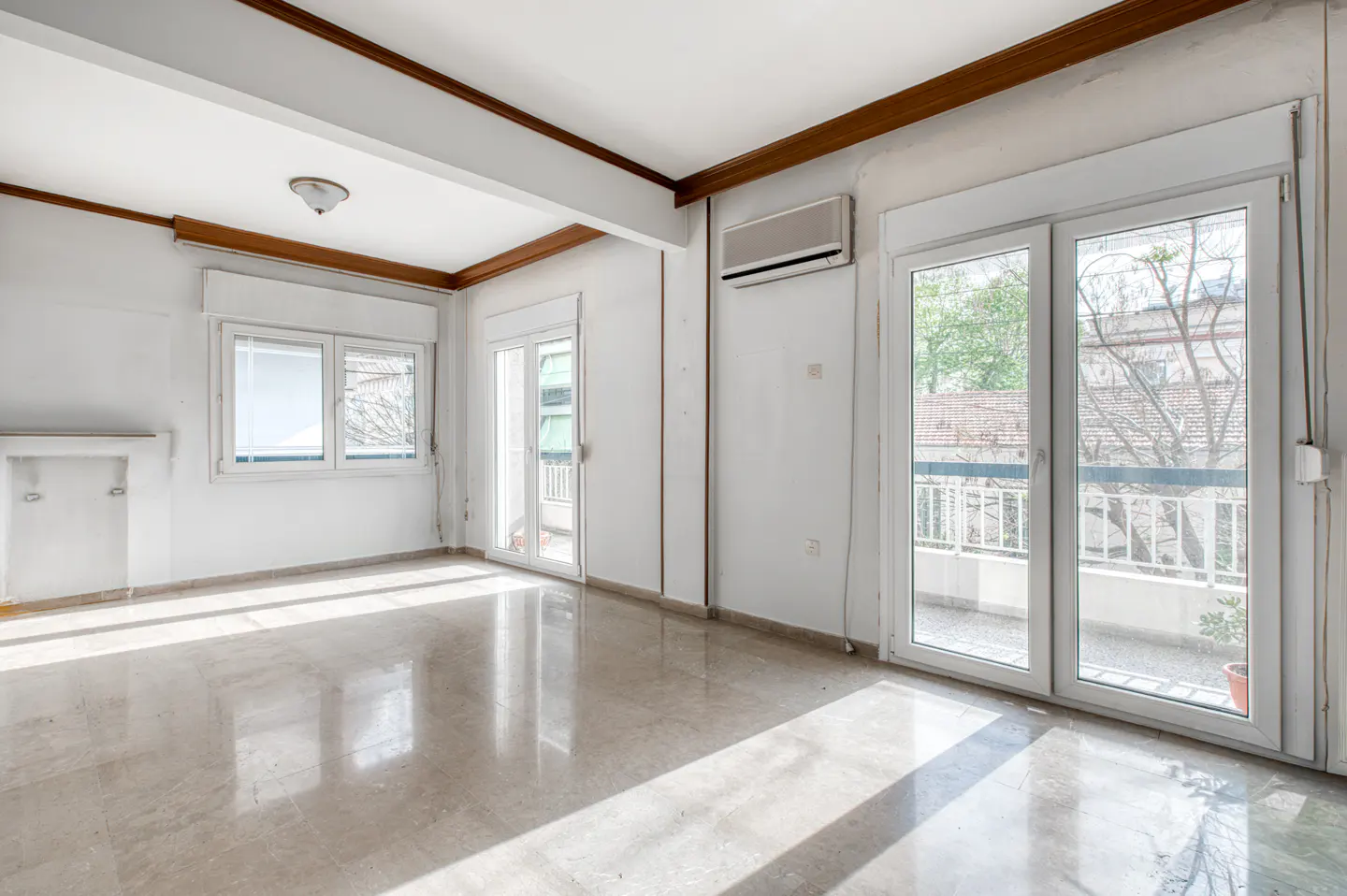 Bright, empty room with marble floors, white walls, and natural light. Windows and balcony doors offer outdoor views.