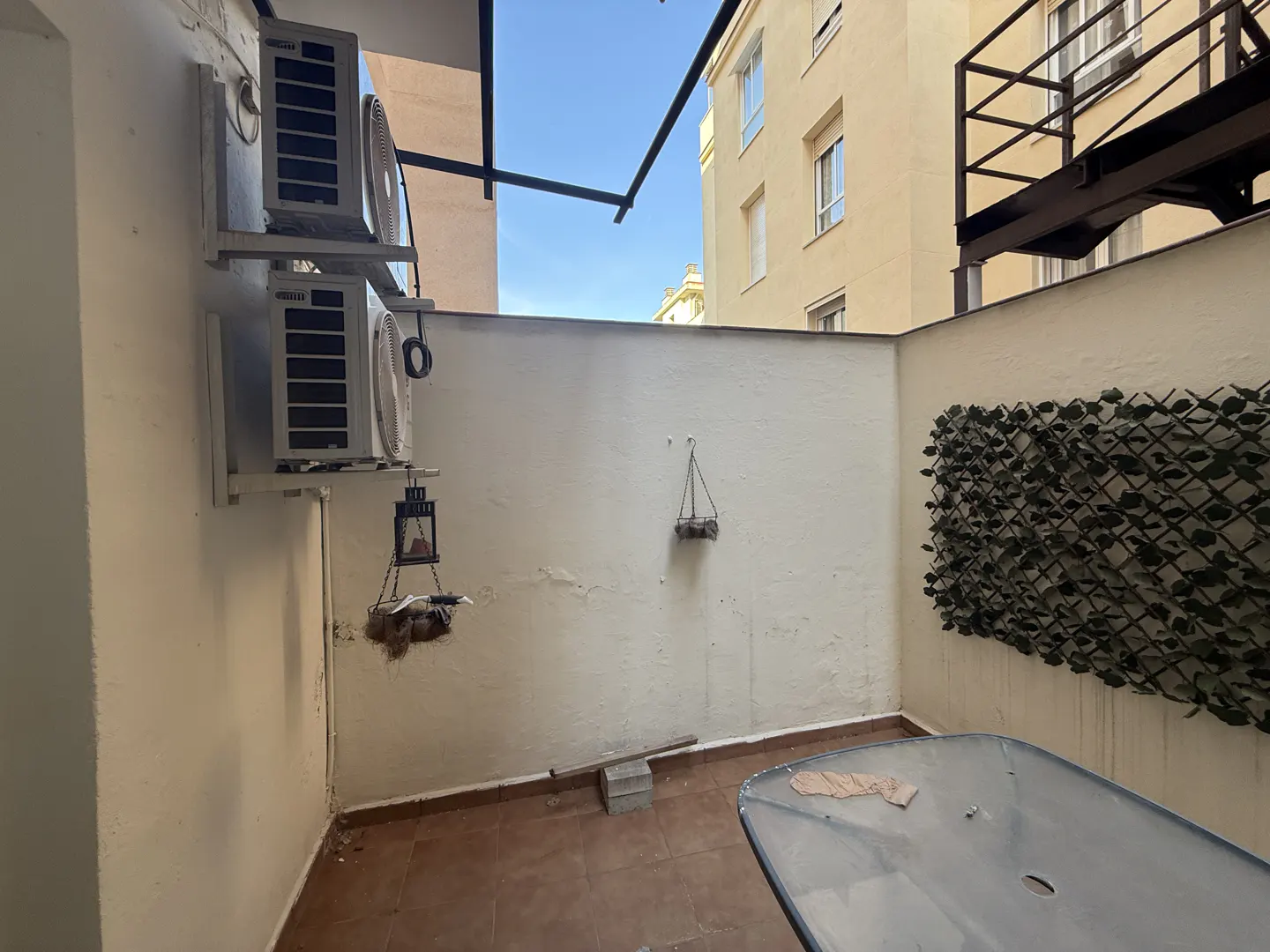 A small outdoor patio with a table, white walls, and two air conditioning units.