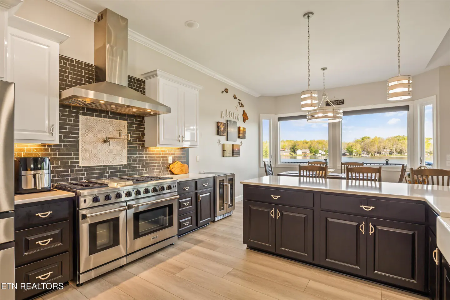 A modern kitchen with stainless steel appliances, dark cabinets, and a large island overlooking a lake.