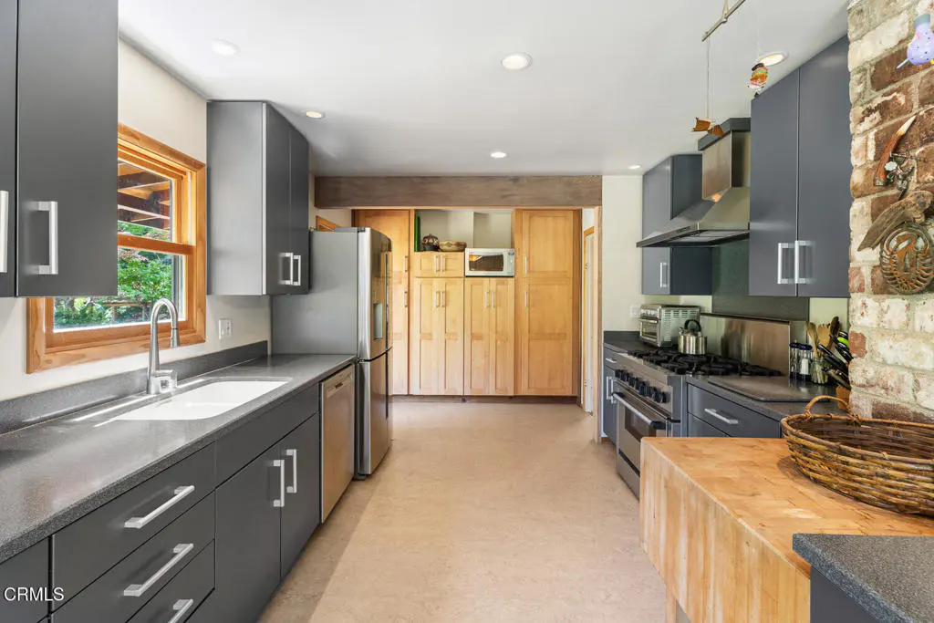 A modern kitchen with gray cabinets, stainless steel appliances, and a butcher block island. A window overlooks greenery.