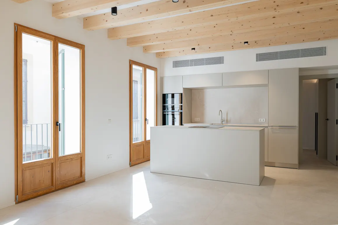 Bright, modern kitchen with white cabinets, island, and wood-beamed ceiling. Two wood-framed glass doors let in natural light.