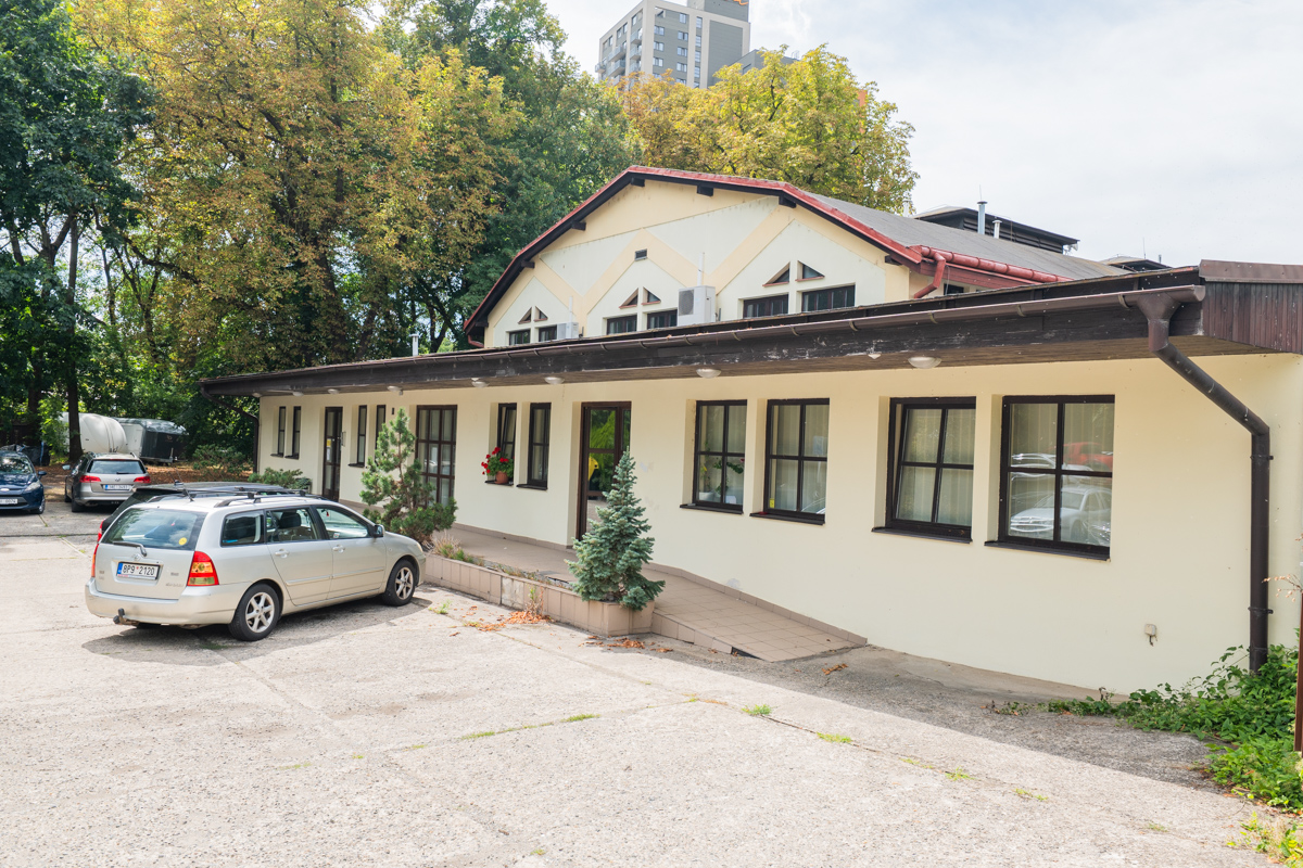 Single-story cream-colored building with a dark roof, a ramp entrance, and a silver station wagon parked in front. [AI-generated text]