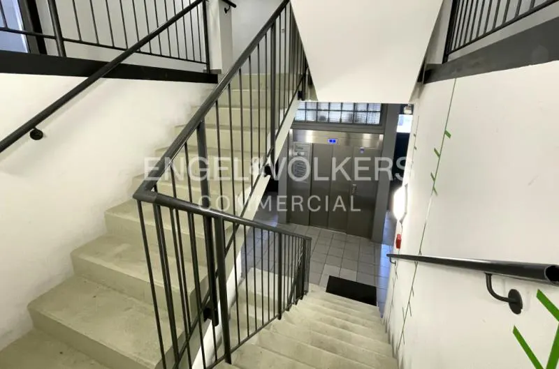 Interior view of a stairwell with concrete stairs, black metal railings, and an elevator in the background.