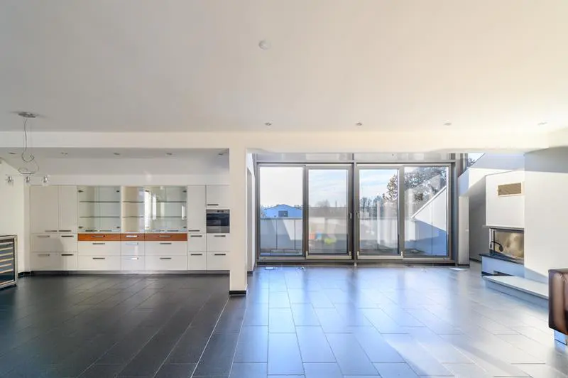 Bright, open-plan living space with black tile flooring, white kitchen cabinets, and sliding glass doors to a balcony. A modern fireplace is visible.