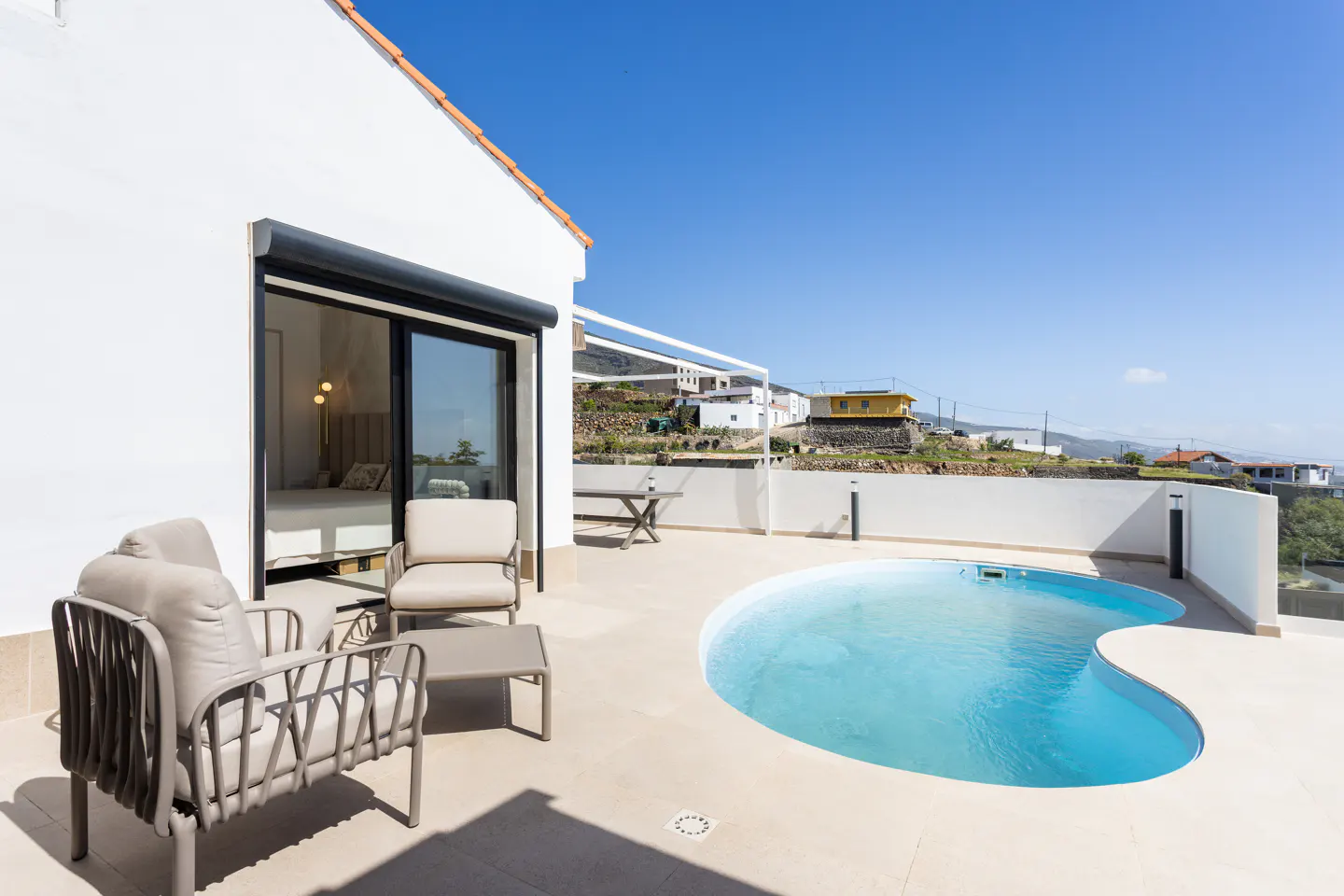 Outdoor patio with a kidney-shaped pool, lounge chairs, and a view of houses on a hill under a clear blue sky.